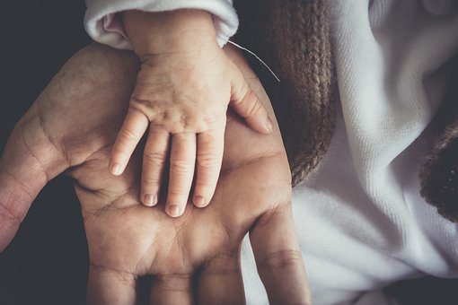 An adult holding a baby's hand in child custody support payments
